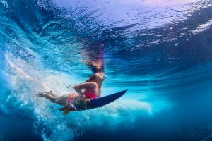 Beautiful surfer girl diving under water with surf board